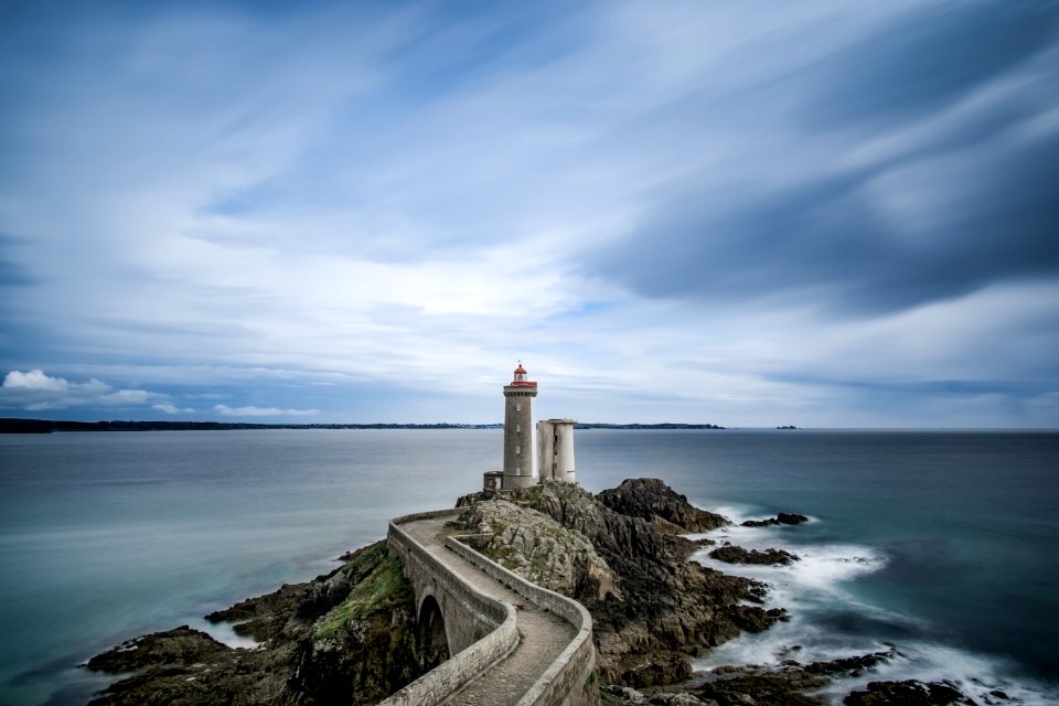 grey concrete lighthouse on cliff surrounded body of water during daytime