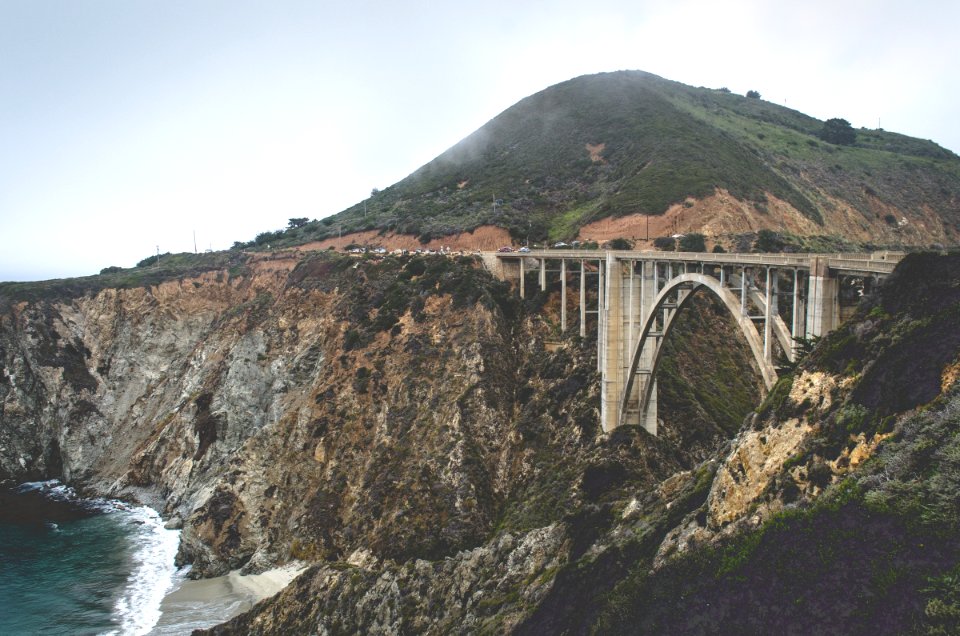 grey concrete bridge between brown and black cliff near body of water during daytime