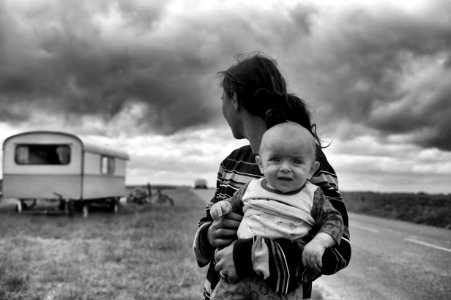 gray scale photography of woman carrying baby looking at camper trailer
