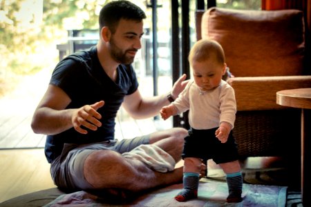 A man helping teach his 1 year old how to walk.
