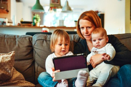 two babies and woman sitting on sofa while holding baby and watching on tablet photo