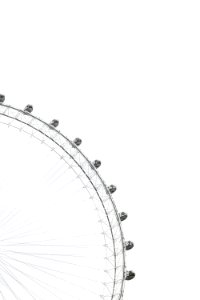 Part of a ferris wheel with enclosed cars for riding in and people in the cars against an overcast sky