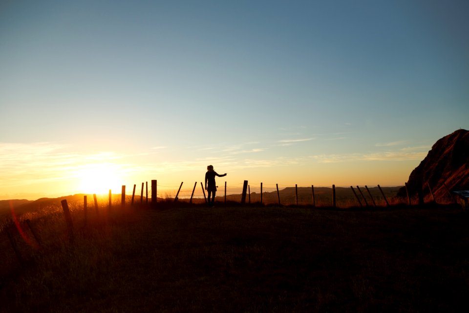 silhouette of man standing in the middle of field facing sunset