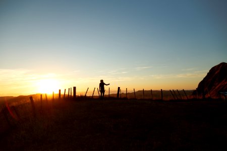 silhouette of man standing in the middle of field facing sunset photo
