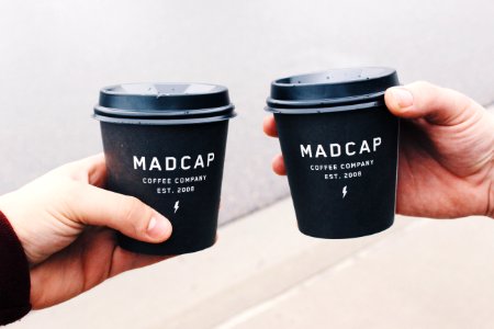 two person holding black Madcap coffee disposable cups photo
