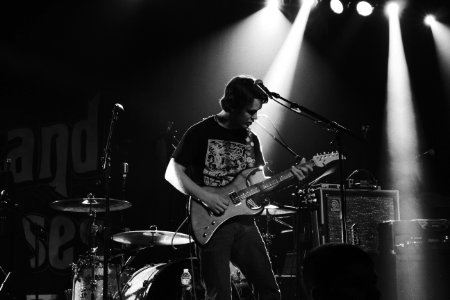 greyscale photo of man playing electric guitar on stage photo
