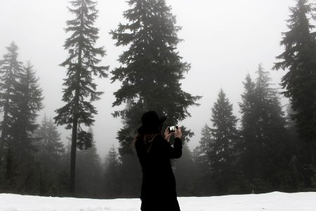 woman takes photo at the snowfield surrounded with trees photo