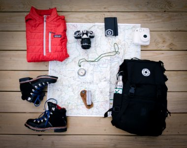 black hiking backpack near white Fujifilm instax mini camera near black leather boots, red half-zip jacket, gray pocket watch on white map photo