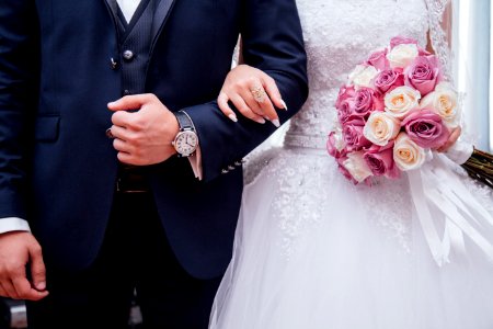 A bride holding a pink and white roses bouquet while holding arms with her husband. photo