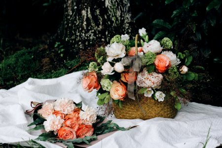 Roses and peonies in a basket and a bouquet on white cloth on the ground photo