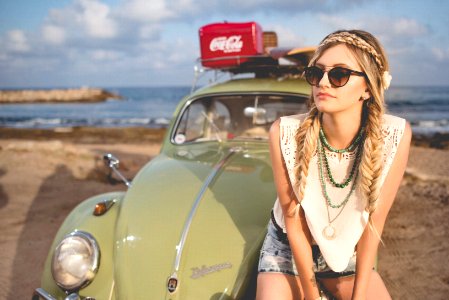 selective focus photography of woman sitting on Volkswagen Beetle parked on beach shore photo