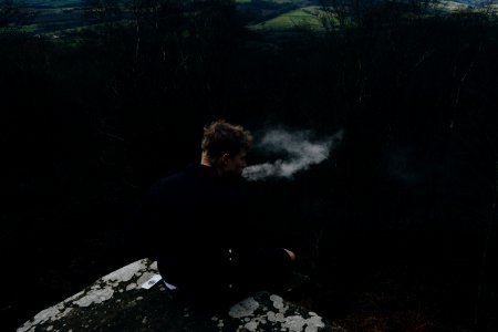 smoking man sitting on rock formation photo