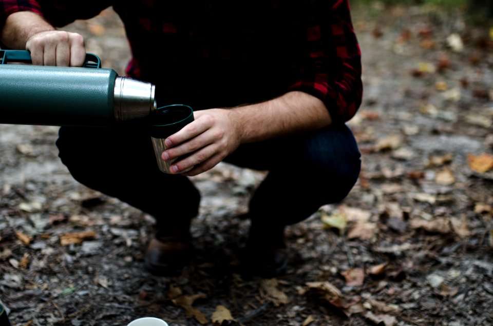 man bending his knees pouring thermal carafe in cup