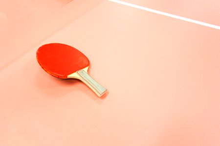 A red table tennis paddle sitting on a court.