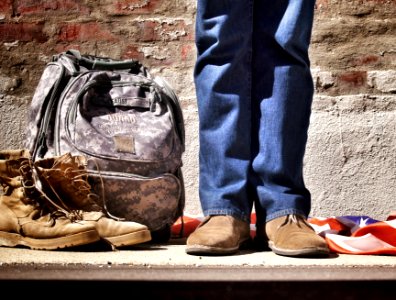 minimalist photography of person standing near backpack and boots photo
