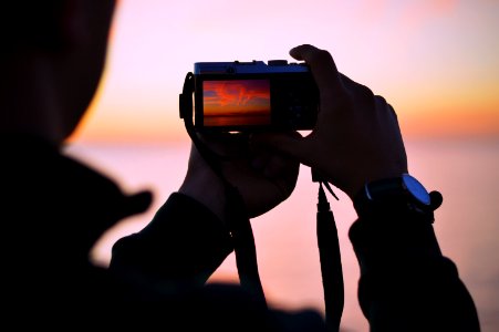 person taking photo of sunset using compact camera photo