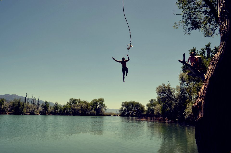 man jumping on body of water with rope