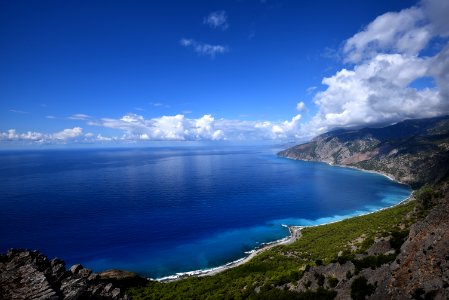 blue ocean water beside mountain under blue and white cloudy sky photo