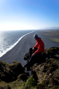 man sitting on mountain cliff near body of water photo