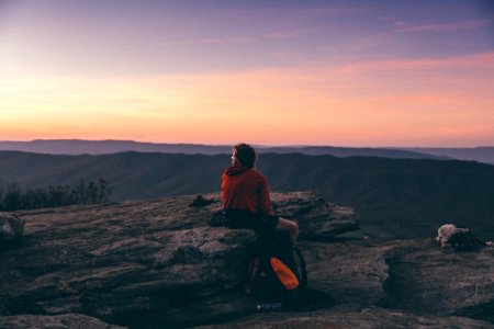 person sitting on boulder overlooking mountain during golden hour photo
