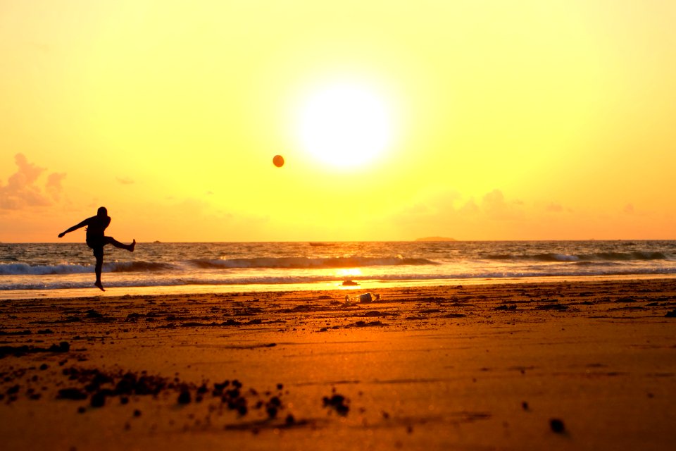 man kicking ball on seashore