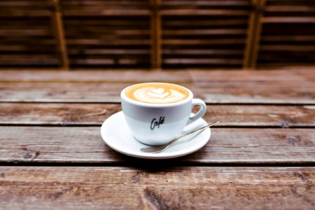 coffee latte on white ceramic saucer beside spoon photo
