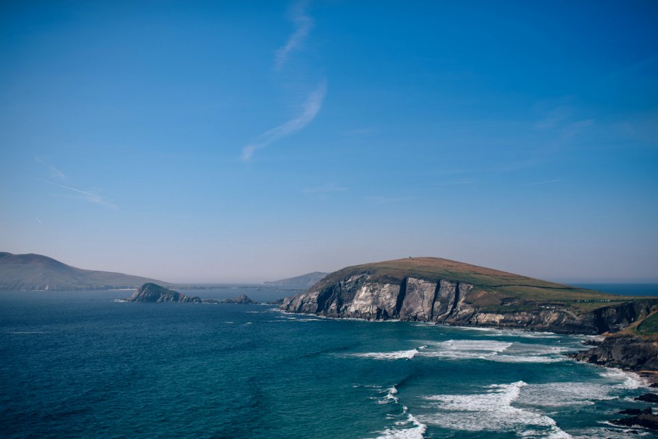 sea waves beside gray and green cliff under clear blue sky during daytime