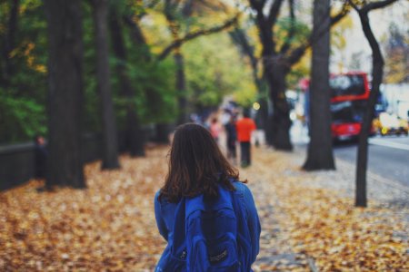 woman with blue backpack on street full of fallen leaves photo