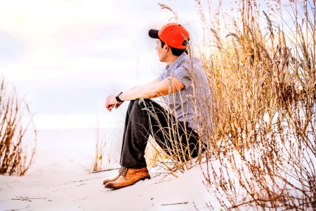 man sitting on sand with wheat looking right during daytime photo