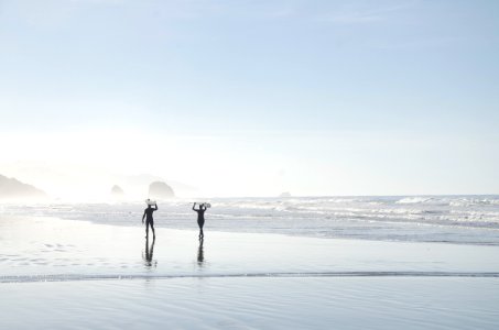 two men carrying surfboards near body of water photo