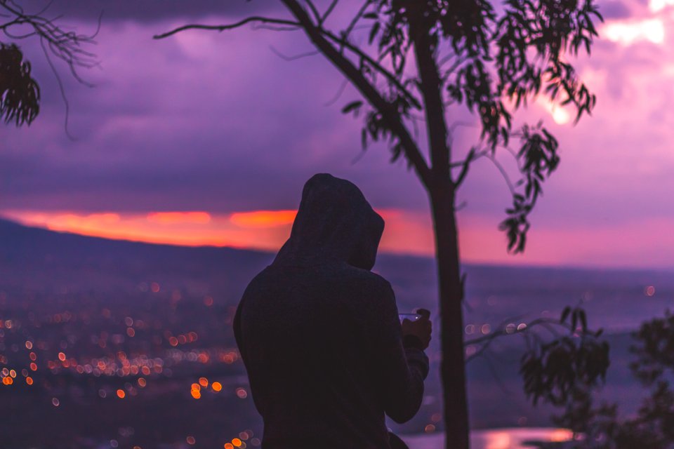 silhouette photo of man standing at the peak facing cityscape