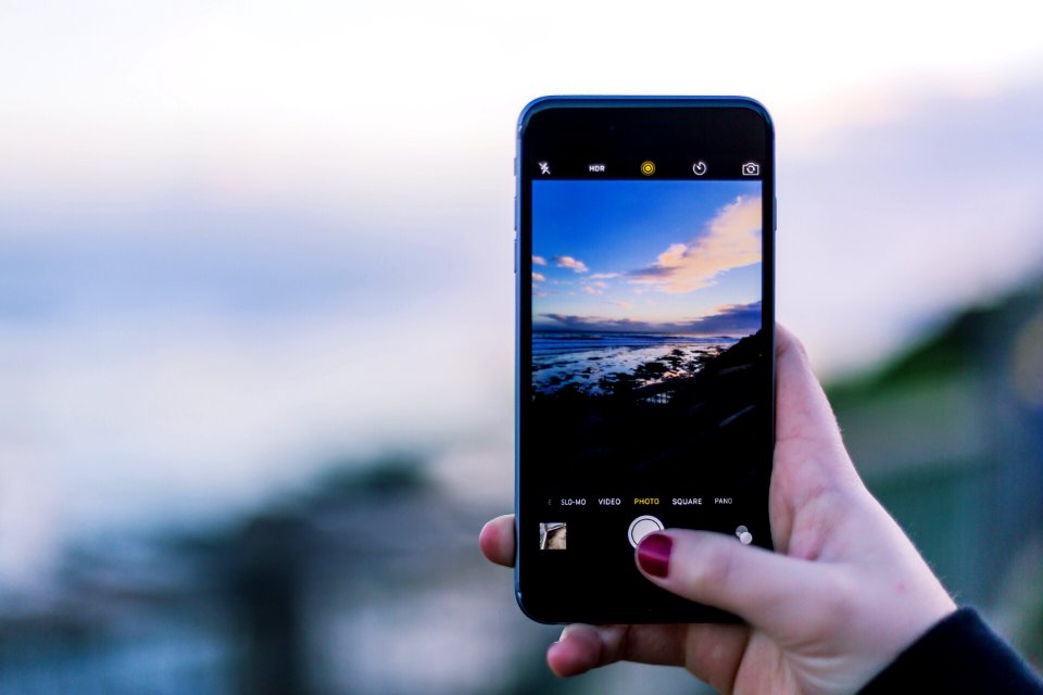A person taking a picture of the ocean under a mostly clear sky.