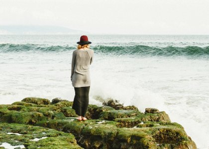 woman standing on green rocks near body of water with waves photo