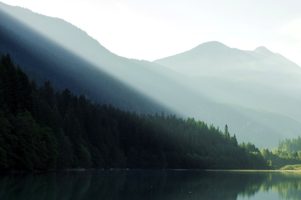 sunlight beaming from mountain top to body of water