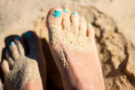 person sky-blue nail polish feet on brown sand photo