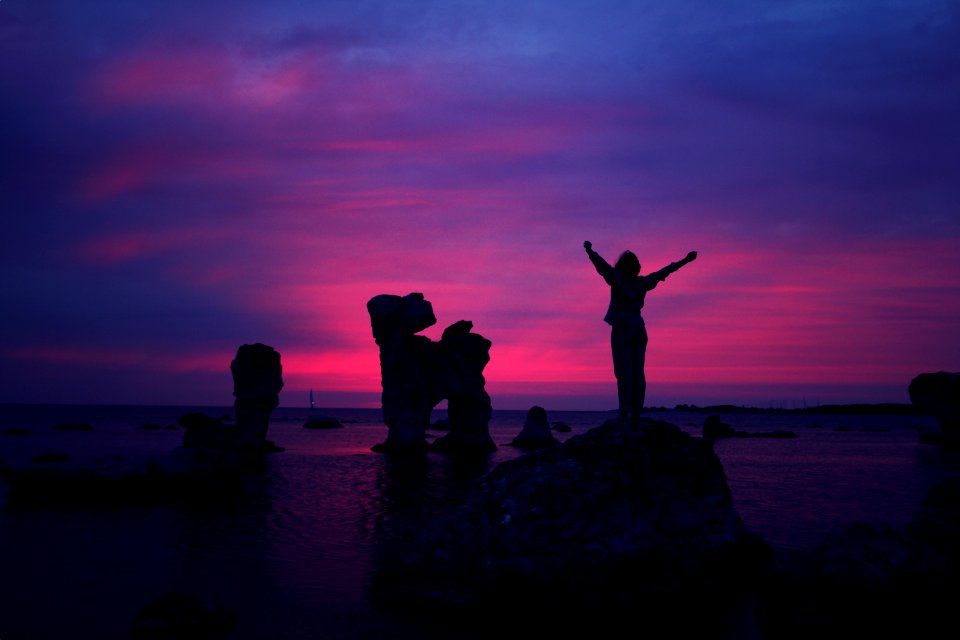 person standing on rock formation with arms in air