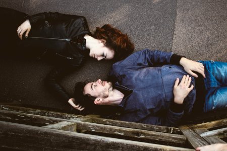 man and woman lying on gray concrete surface looking at each other photo