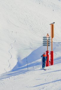 man in blue jacket holding ski poles standing near red and brown post photo