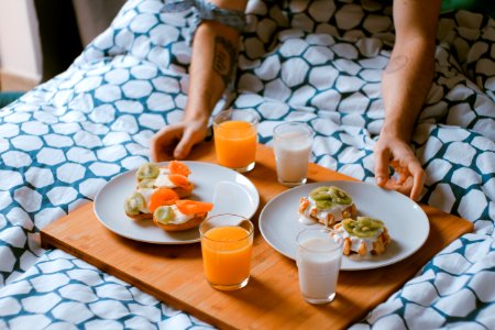 person serving pastries on white ceramic plates with fruit juice glasses on wooden tray on top of bed photo
