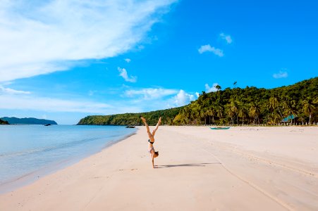 woman doing acrobatic on seashore near mountain range under cumulus clouds
