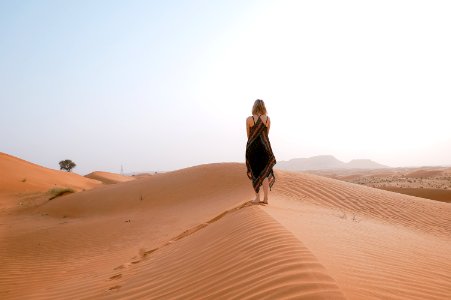woman walking on desert during daytime photo