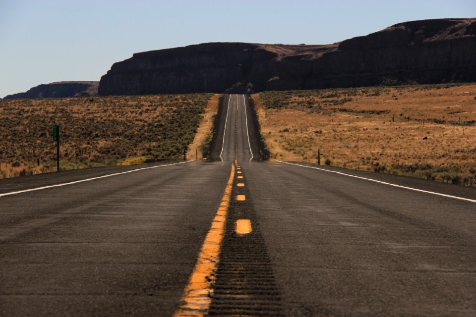 gray asphalt road between brown grass field during daytime