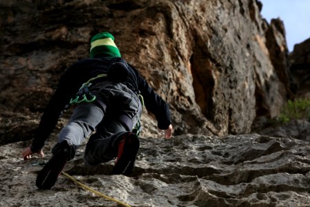 man in black jacket and green pants climbing on brown rocky mountain during daytime photo