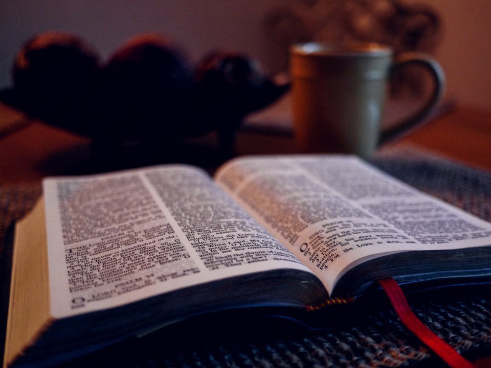 open book on black mat beside grey ceramic mug