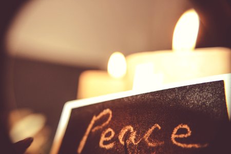 Peace, written on a black chalkboard with white chalk in front of candles.