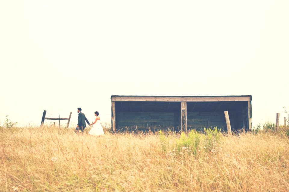 Wedding day photo in a field beside an old wooden farm building