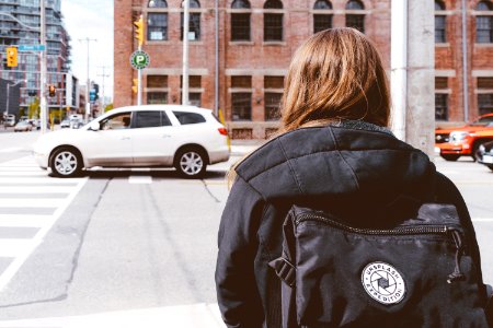 woman in black hooded jacket standing beside street near white SUV photo