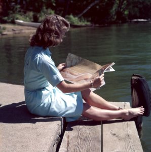 woman wearing blue dress reading magazine near body of water during daytime photo
