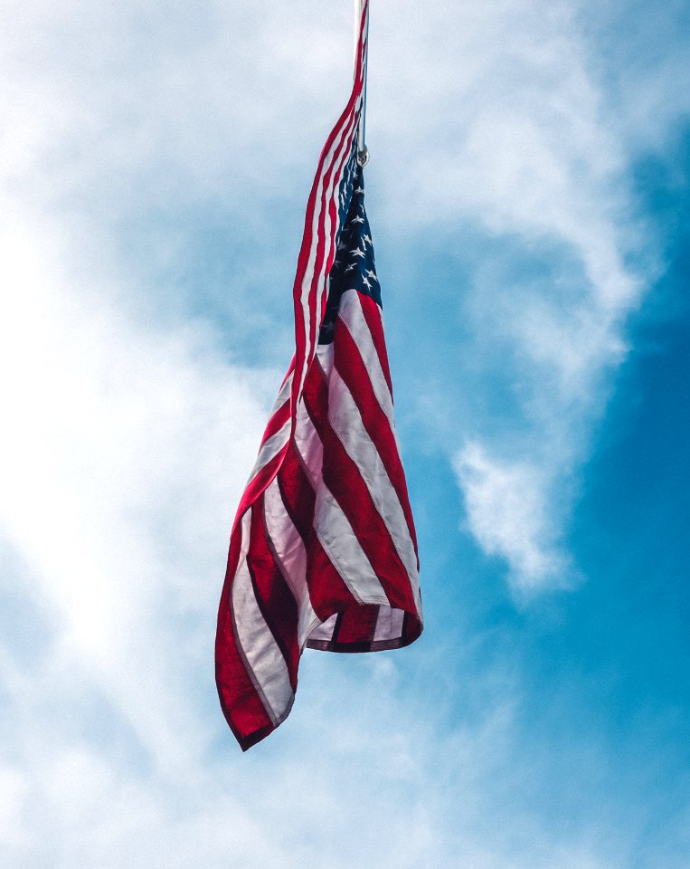flag of the United State flying under white clouds