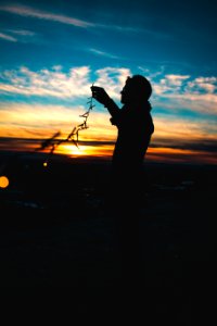 silhouette of person holding string lights during sunset photo